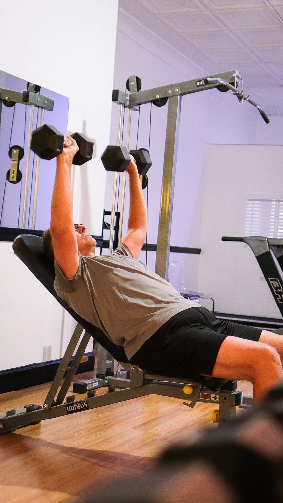 Caldwell client benchpressing with personal Trainer